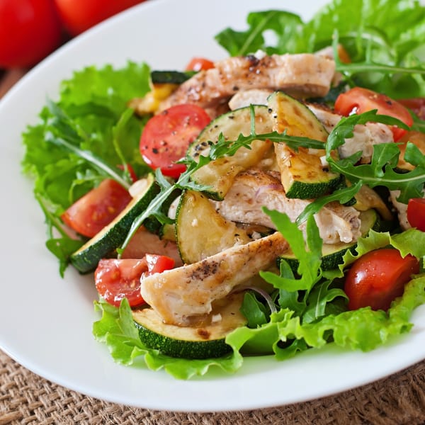 Grilled chicken and zucchini salad with cherry tomatoes and arugula on a white plate.
