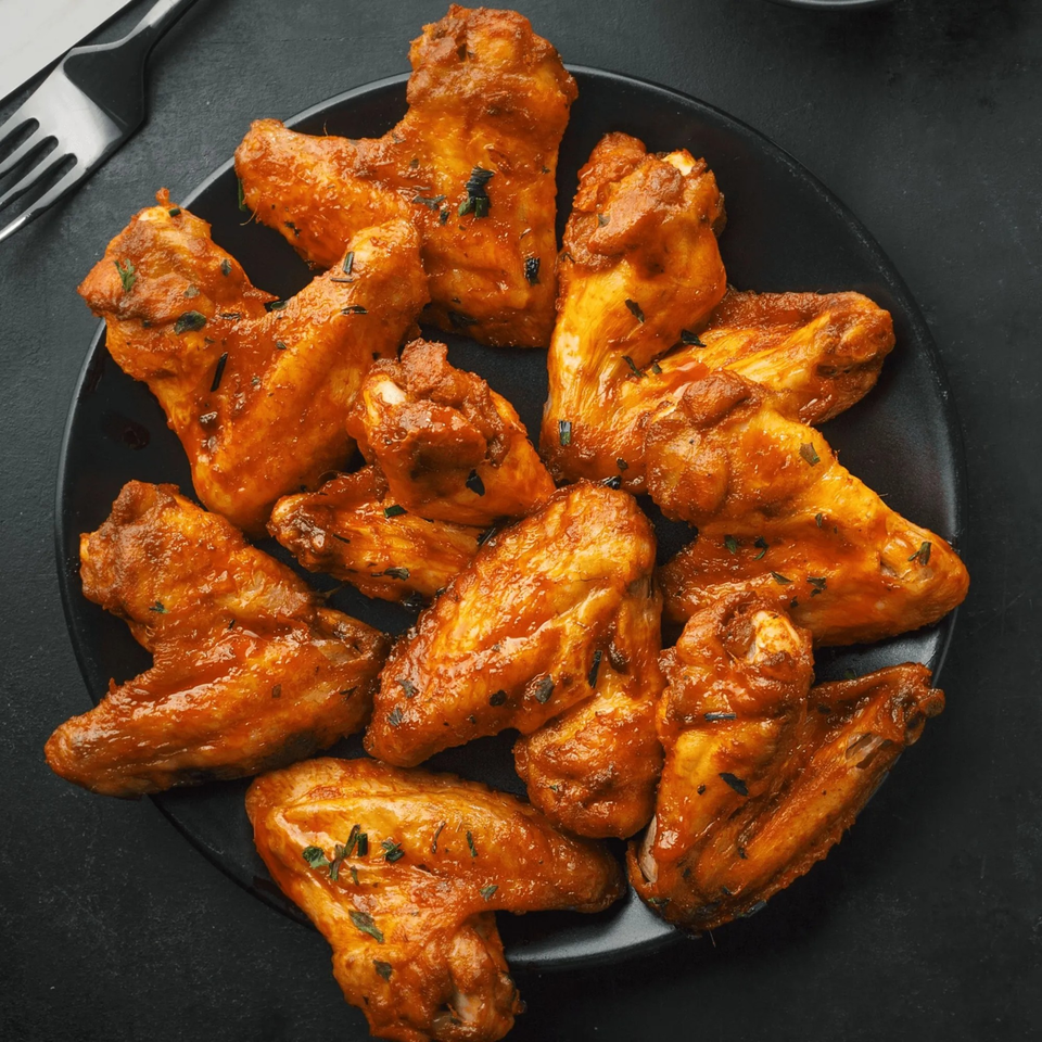 A black plate filled with Angelo's Pizza & Subs' chicken wings, coated in a spicy orange sauce.
